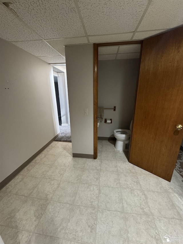 bathroom featuring toilet, tile patterned floors, a paneled ceiling, and baseboards