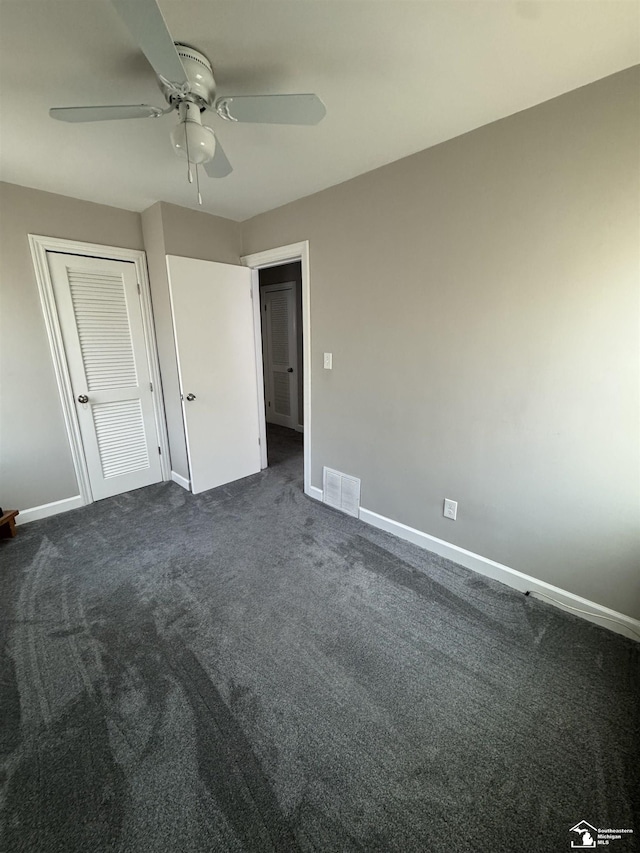 unfurnished bedroom with baseboards, visible vents, ceiling fan, dark carpet, and a closet