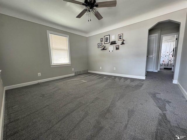 spare room featuring baseboards, visible vents, a ceiling fan, arched walkways, and dark carpet