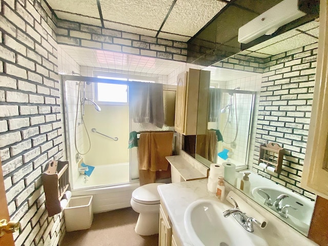 bathroom featuring brick wall, enclosed tub / shower combo, vanity, and toilet