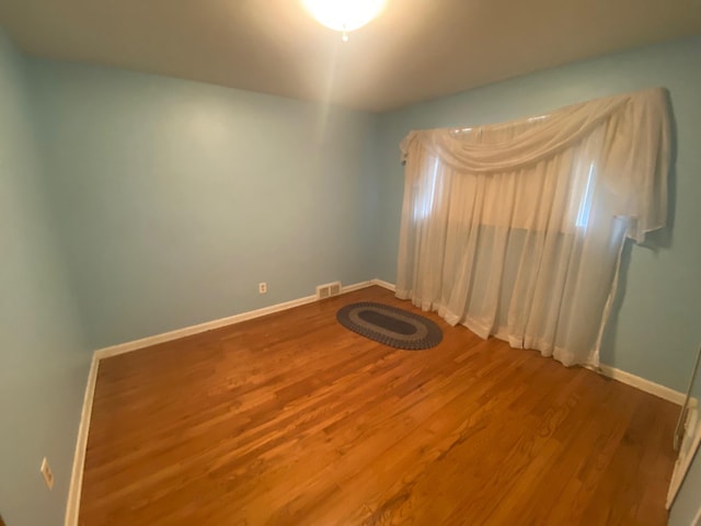 spare room with baseboards, visible vents, and wood finished floors