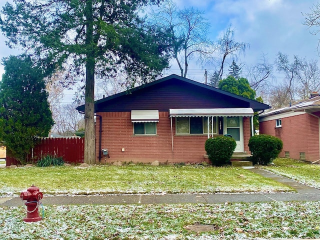 bungalow-style home featuring brick siding, a front lawn, and fence