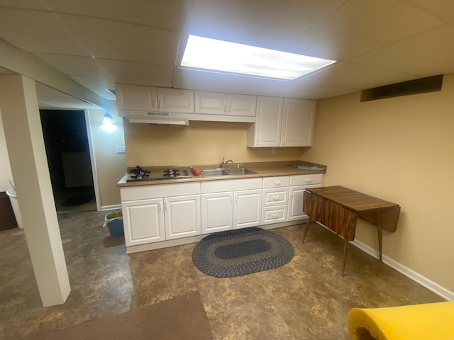 kitchen featuring a paneled ceiling, under cabinet range hood, a sink, white cabinetry, and cooktop