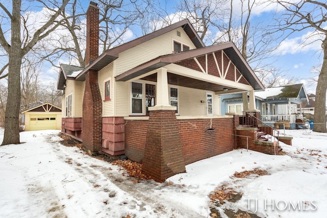 view of front facade featuring an outbuilding, brick siding, a chimney, a porch, and a garage