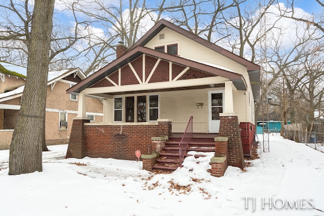 view of front of home with covered porch, brick siding, a chimney, and fence