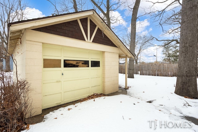 snow covered garage with a garage and fence