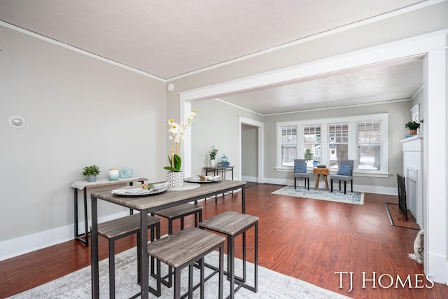 dining space with baseboards, a fireplace, ornamental molding, and wood finished floors