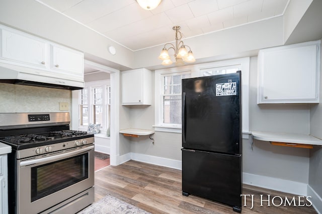 kitchen featuring under cabinet range hood, stainless steel range with gas cooktop, white cabinetry, and freestanding refrigerator