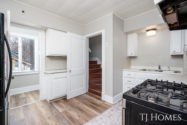 kitchen featuring black appliances, range hood, light wood-style floors, and a sink