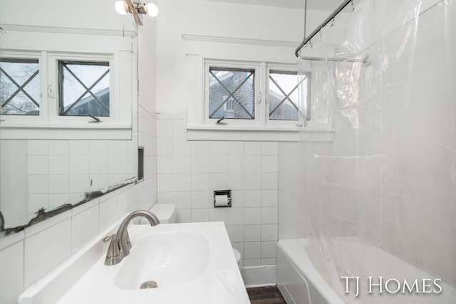 bathroom featuring toilet, a sink, a wealth of natural light, and tile walls