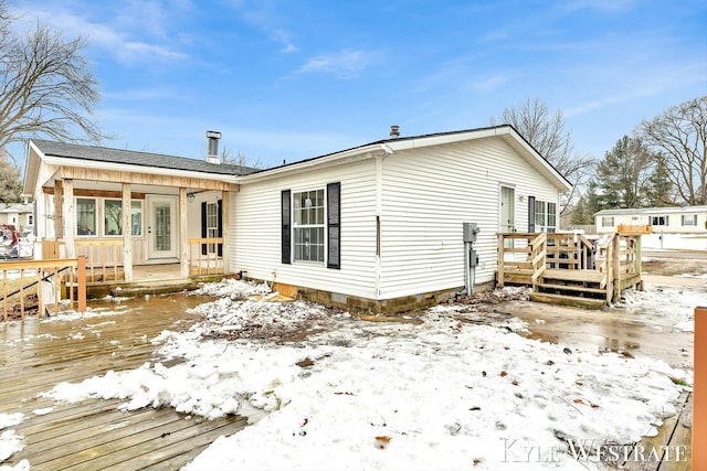 snow covered back of property with a wooden deck