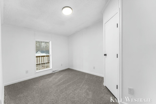 spare room featuring baseboards, visible vents, dark carpet, and a textured ceiling