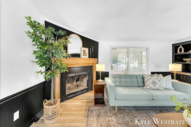 living room with a textured ceiling, wood finished floors, wainscoting, and a fireplace