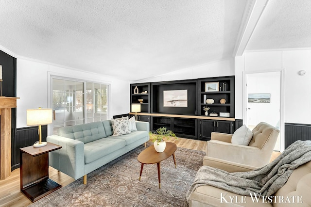 living room featuring a wainscoted wall, vaulted ceiling with beams, a textured ceiling, and light wood finished floors