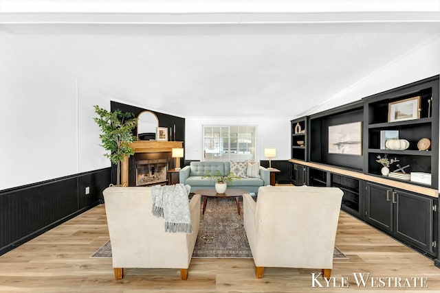 living room with built in features, a glass covered fireplace, a decorative wall, and light wood finished floors