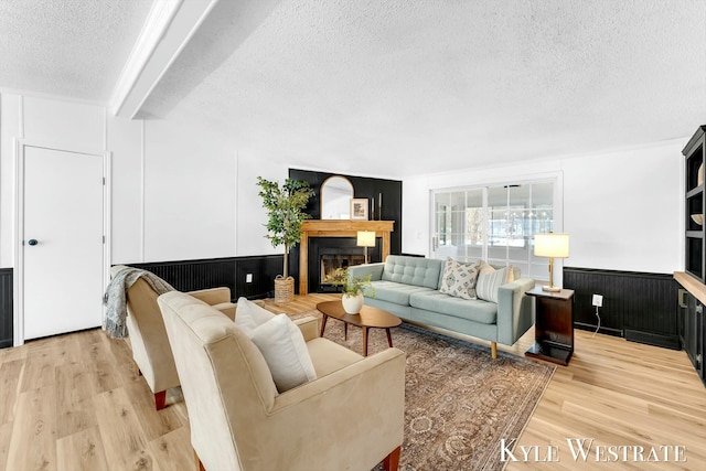 living area with a glass covered fireplace, a wainscoted wall, light wood-style flooring, and a textured ceiling