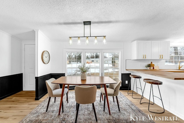 dining area with light wood-type flooring, a wainscoted wall, crown molding, and a textured ceiling