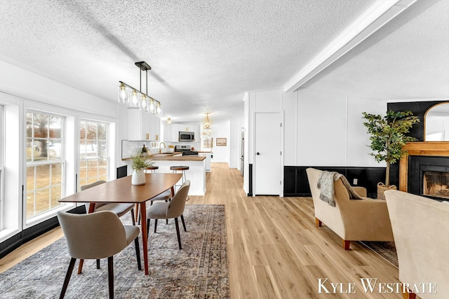 dining area with light wood-type flooring, beam ceiling, a textured ceiling, and a glass covered fireplace