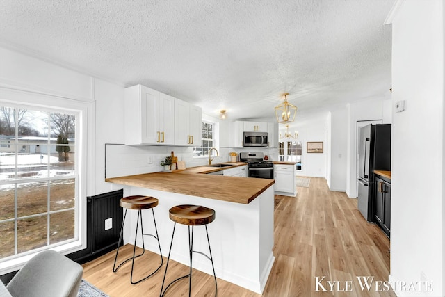 kitchen with white cabinets, a peninsula, stainless steel appliances, light wood-style floors, and a sink