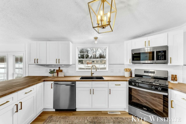 kitchen featuring decorative backsplash, butcher block counters, light wood-style flooring, appliances with stainless steel finishes, and a sink