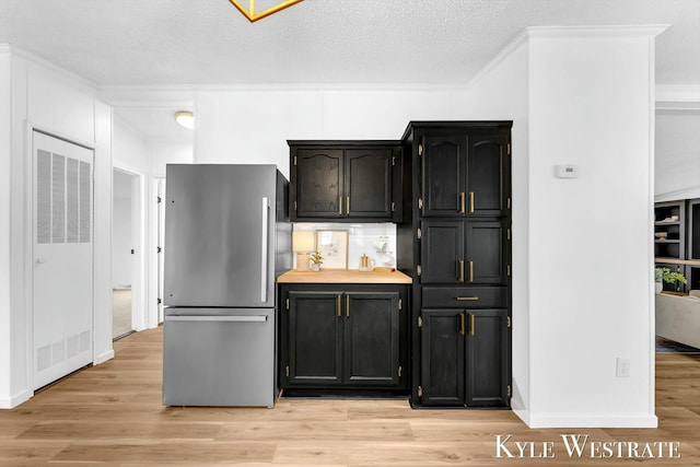 kitchen with dark cabinetry, light wood-style flooring, freestanding refrigerator, and crown molding