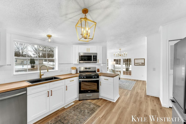 kitchen featuring a notable chandelier, stainless steel appliances, decorative backsplash, a sink, and butcher block countertops