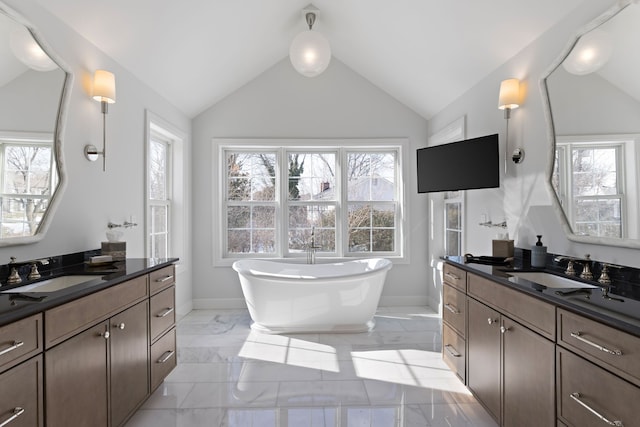 bathroom featuring vaulted ceiling, marble finish floor, a freestanding bath, and a sink