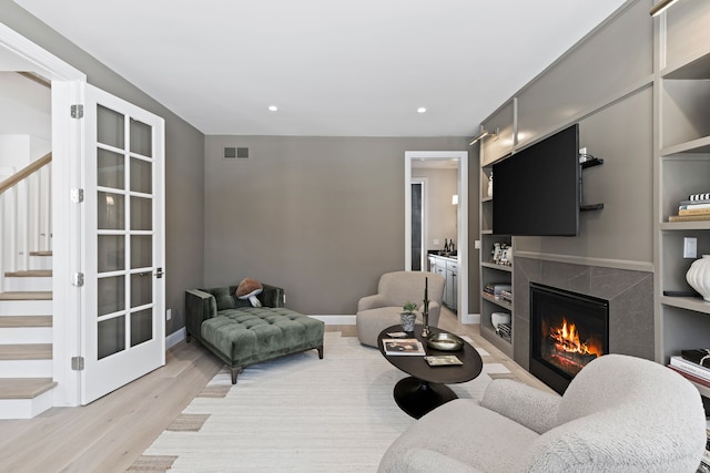 living room featuring a high end fireplace, visible vents, baseboards, stairway, and light wood finished floors