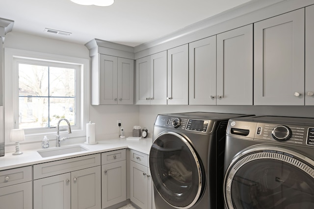 laundry area featuring washing machine and dryer, cabinet space, a sink, and visible vents