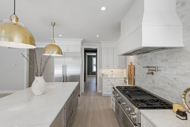 kitchen with cooktop, white cabinets, custom range hood, light stone countertops, and backsplash