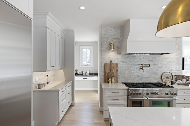 kitchen featuring range with two ovens, light stone counters, white cabinetry, light wood-style floors, and custom range hood