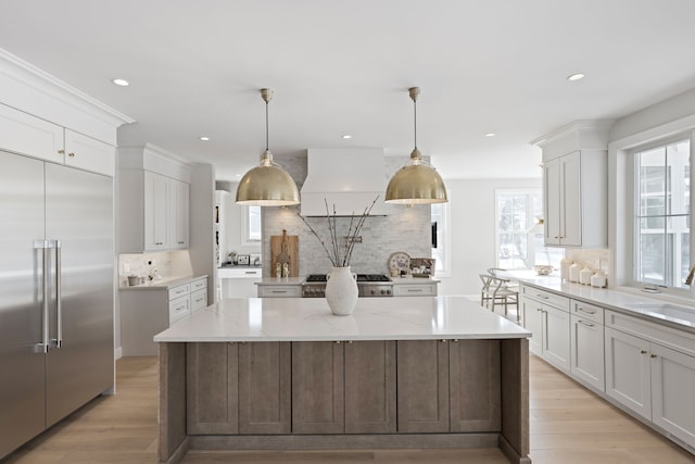 kitchen with built in fridge, a center island, light wood-style flooring, white cabinetry, and wall chimney exhaust hood