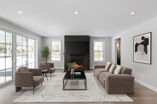 living area with light wood-style floors, baseboards, a large fireplace, and recessed lighting