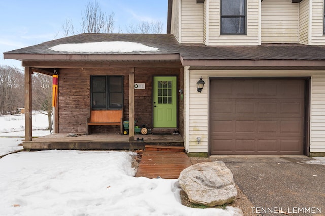 snow covered property entrance featuring a garage, a shingled roof, and a porch