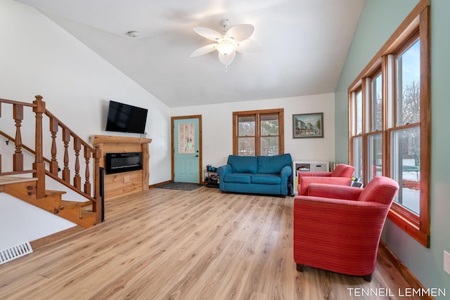 living room with lofted ceiling, plenty of natural light, wood finished floors, and a glass covered fireplace