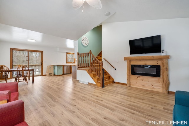 living area featuring baseboards, a glass covered fireplace, lofted ceiling, wood finished floors, and stairs