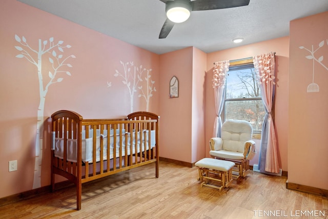 bedroom with a ceiling fan, a crib, baseboards, and wood finished floors