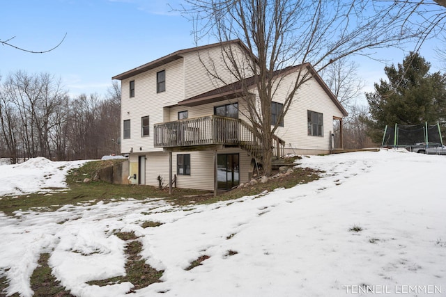 snow covered back of property with a trampoline and a wooden deck