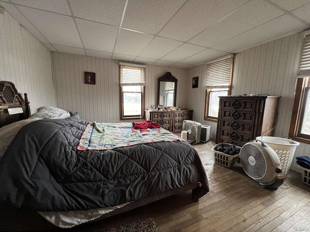 bedroom featuring hardwood / wood-style floors, a drop ceiling, and wallpapered walls