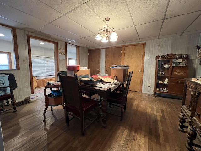 dining space featuring dark wood-style floors, a drop ceiling, and an inviting chandelier