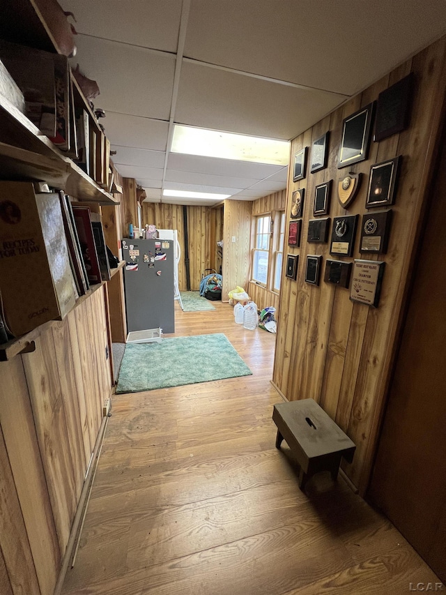 corridor featuring a drop ceiling, wood walls, and light wood-style flooring