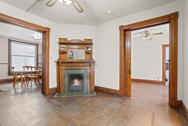 living area featuring a ceiling fan, baseboards, a tiled fireplace, and wood finished floors