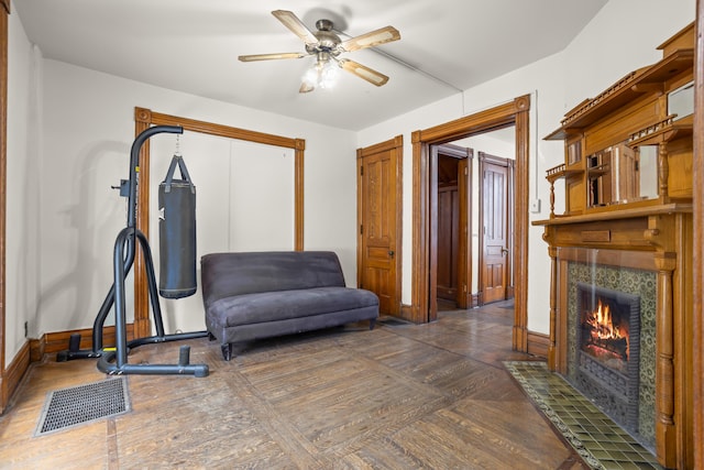 exercise area with wood finished floors, a ceiling fan, visible vents, baseboards, and a tiled fireplace