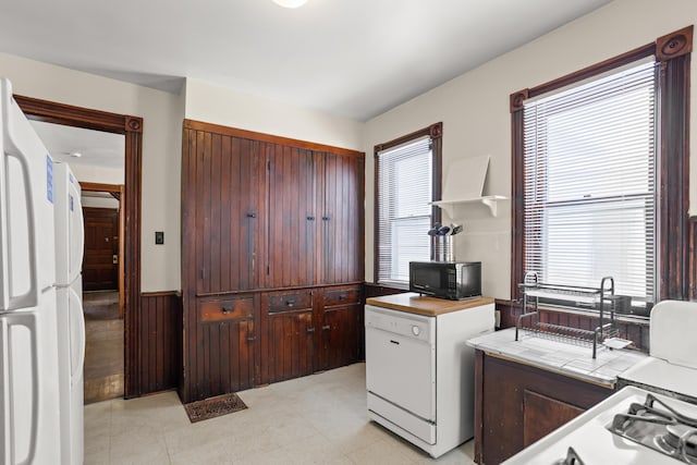 kitchen featuring tile countertops, white appliances, and a wainscoted wall