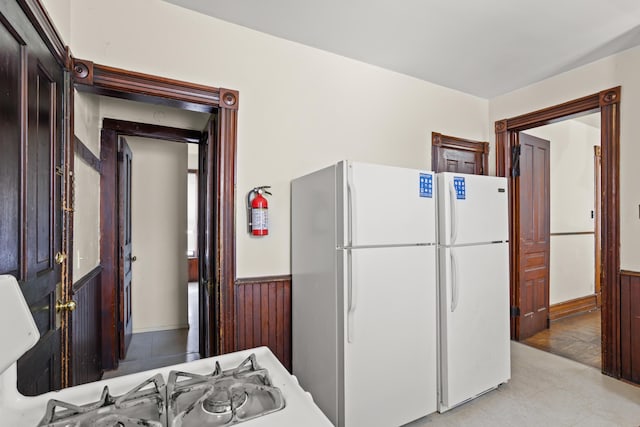 kitchen featuring a wainscoted wall, wooden walls, and freestanding refrigerator