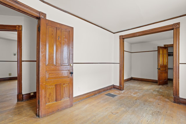 empty room featuring ornamental molding, visible vents, baseboards, and hardwood / wood-style flooring