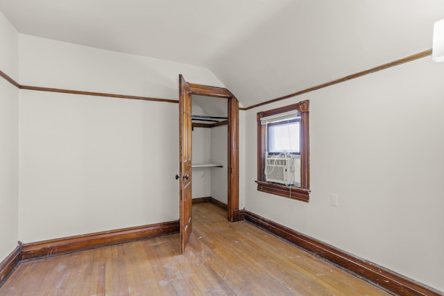 unfurnished bedroom featuring cooling unit, hardwood / wood-style flooring, baseboards, vaulted ceiling, and a closet