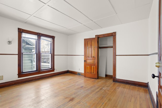 unfurnished bedroom with baseboards, a closet, a paneled ceiling, and light wood-style floors