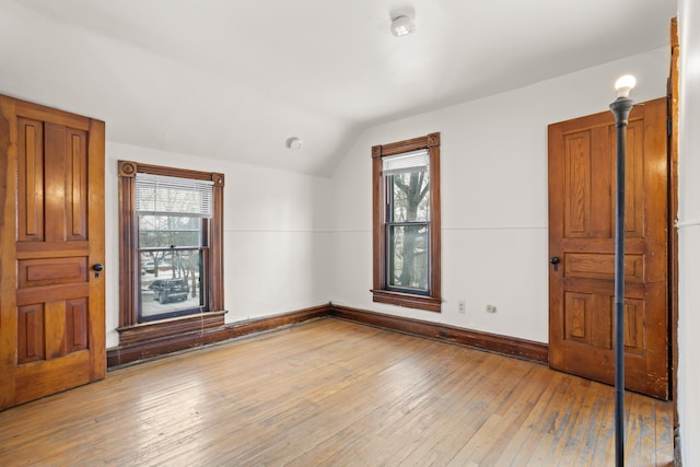 spare room with vaulted ceiling, light wood-style flooring, and baseboards