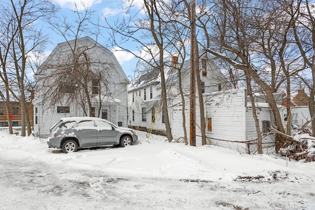 view of snowy exterior with a garage and a gambrel roof